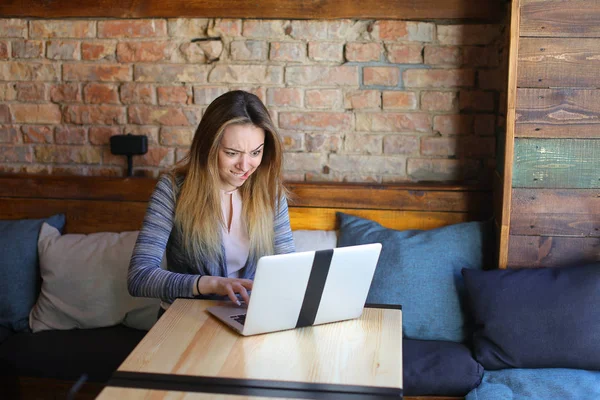 Молодая женщина сидит в уютной кофейне рядом со столом со стеклянной чашкой капучино и болтает с помощью ноутбука . — стоковое фото
