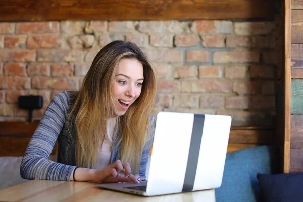 Mujer riendo usando el ordenador portátil en la cafetería con fondo de pared de ladrillo . — Foto de Stock
