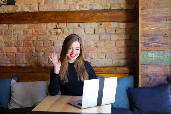 Mujer haciendo videollamada por computadora portátil en la cafetería y saludando la mano . — Foto de Stock