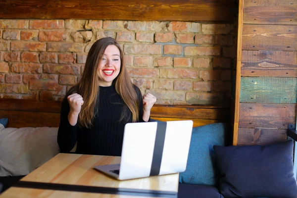 Chica feliz disfrutando de ganar apuestas en línea por ordenador portátil en la cafetería . — Foto de Stock