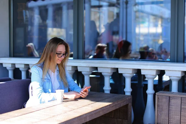 Mujer joven descansando en la cafetería de la calle con smartpnone en caso de color rosa . — Foto de Stock