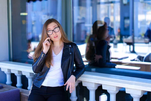 Jocund mulher vestindo óculos e falando por smartphone no café de rua . — Fotografia de Stock
