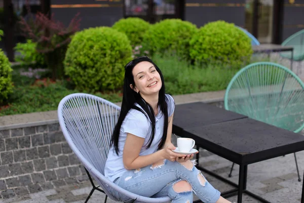 Alegre persona femenina sentada en la silla en la cafetería cerca de las plantas verdes y beber café . — Foto de Stock