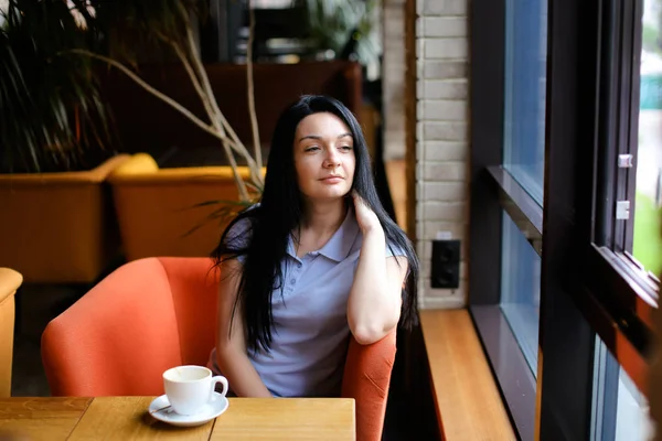 커피 한잔과 함께 카페에서 오렌지 안락의자에 앉아 갈색 머리 여자. — 스톡 사진