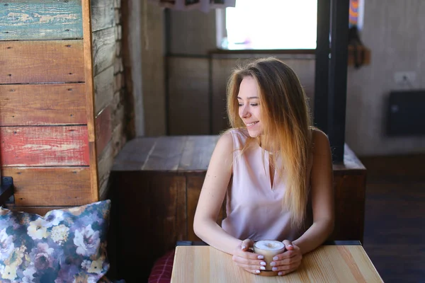 Dziewczyna siedzi w kawiarni w pobliżu stół szkło filiżankę kawy i komunikowanie się przy użyciu smartfona. — Zdjęcie stockowe