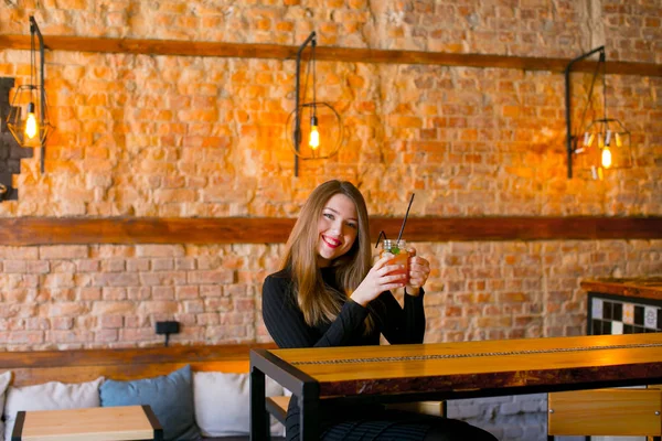 Chica satisfecha sentada cerca de la mesa de madera con taza de limonada en la cafetería y relajante . — Foto de Stock