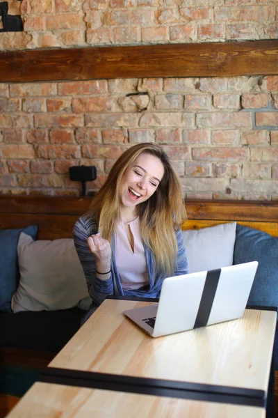 Beautiful female sitting near wooden table with white laptop and cup of coffee in cozy cafe.