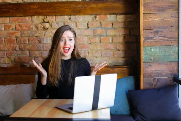 Disappointed female person using laptop and sitting at cafe.