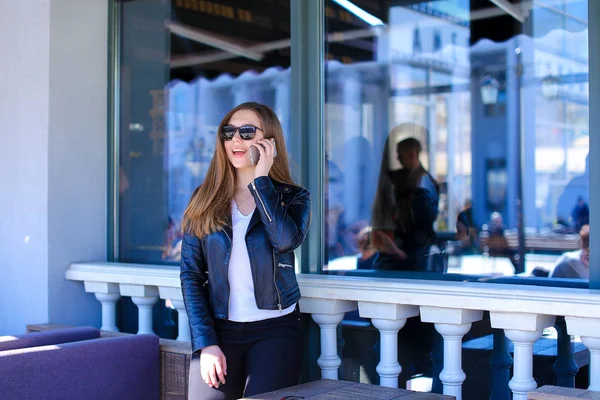 Menina agradável em óculos de sol falando por smartphone no café de rua . — Fotografia de Stock