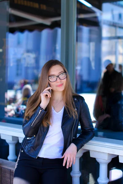 Чарівна жінка в окулярах розмовляє по смартфонах у вуличному кафе . — стокове фото