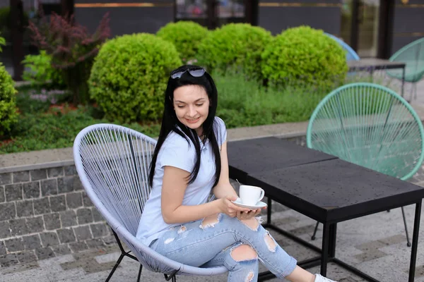 Bonita pessoa feminina sentada na cadeira no café perto de plantas verdes e beber café . — Fotografia de Stock