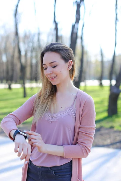 Красива дівчина ходить в парку і використовує розумний годинник . — стокове фото