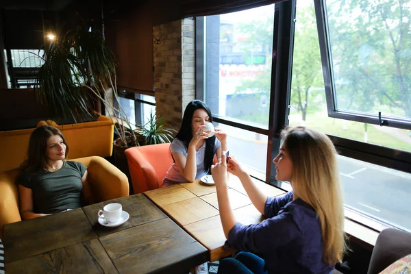 Unge kvinnelige venner som snakker på kafeen og bruker smarttelefon til bilder, drikker kaffe . – stockfoto