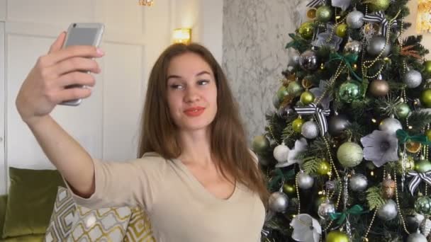 Slow motion lärare tjej tar selfies nära nyår träd med smartphone. — Stockvideo
