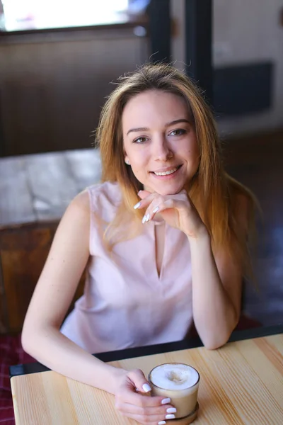 Feminino sentado em café acolhedor perto de mesa de madeira com xícara de café . — Fotografia de Stock