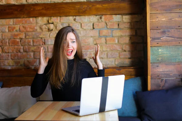 Shocked female person using laptop and sitting at cafe.