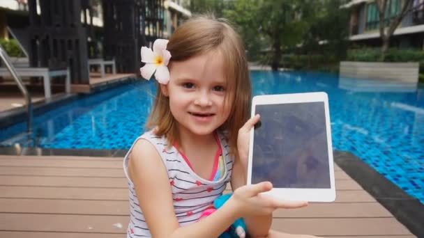 Niña mostrando selfie en la tableta y sentada cerca de la piscina . — Vídeos de Stock