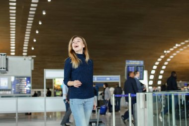 Boyun yastığı ile Havaalanı Salonu'nda valiz üzerinde genç kadın.