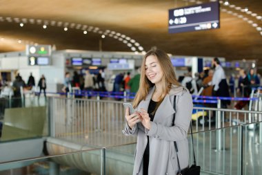 Güzel kadın smartphone vasıl Havaalanı, mesaj yazmaya bir palto giyiyor.