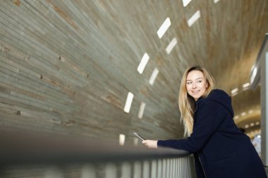 Modern smartphone ile tek sesli ışıklı arka planda duran sarışın kız öğrenci.