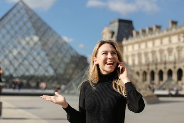 Siyah elbise Paris Louvre ve cam pyramind duran, smartphone tarafından konuşan genç kadın.