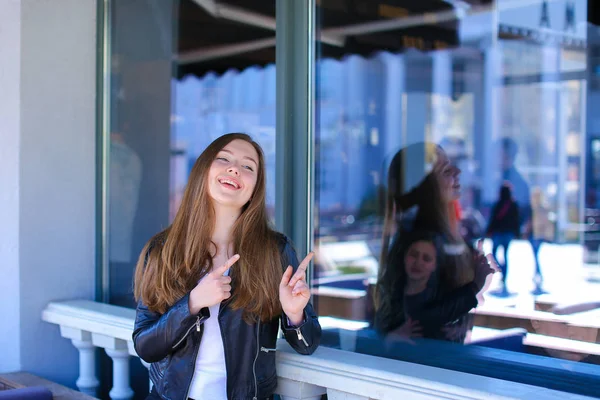 Jeune fille debout près de la fenêtre du café de rue avec des index . — Photo