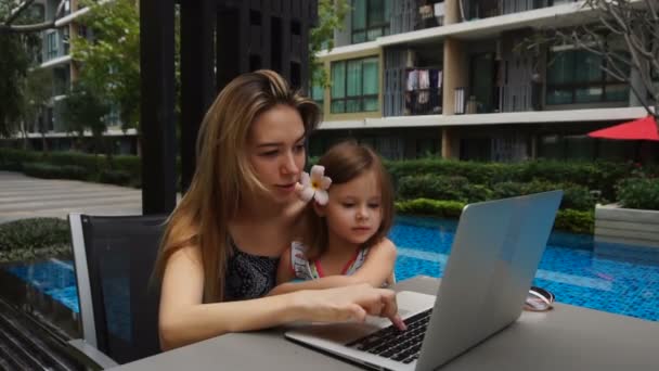 Junge Mutter mit kleiner Tochter plaudert in Zeitlupe am Laptop in Schwimmbadnähe. — Stockvideo