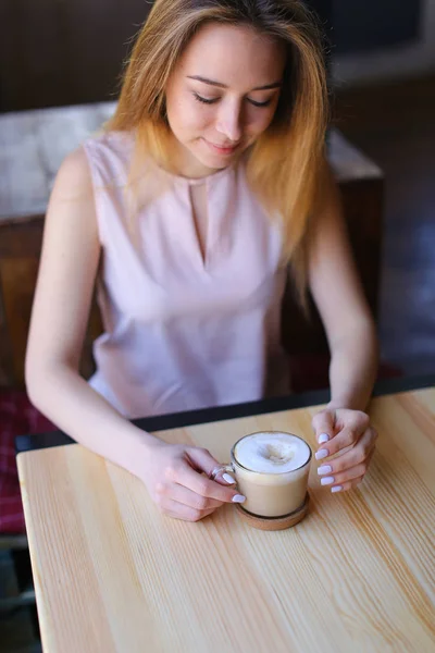 Młoda kobieta siedzi w przytulnej kawiarni z filiżanki cappuccino i pozowanie do zdjęć do pamięci. — Zdjęcie stockowe