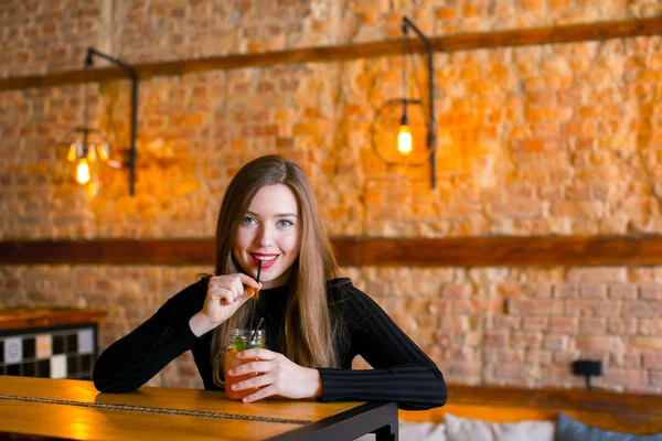 Удовлетворенная девушка сидит у деревянного стола с чашкой лимонада в кафе и расслабляется . — стоковое фото