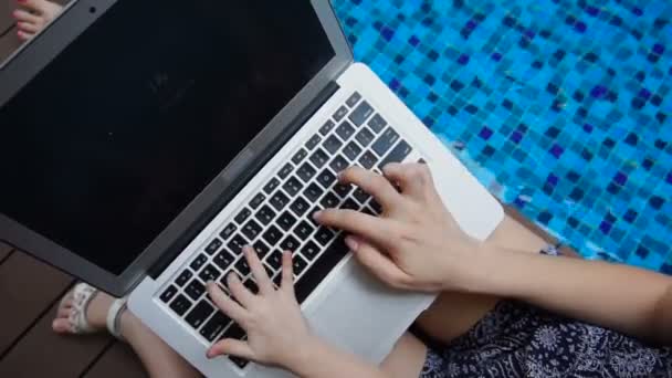 Nahaufnahme Schreibmaschine auf Laptop-Tastatur in der Nähe des blauen Swimmingpools. — Stockvideo