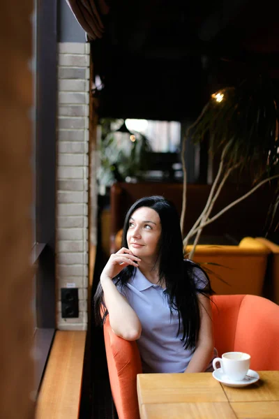 Young woman sitting in orange arm chair at cafe with cup of coffee. — Stock Photo, Image