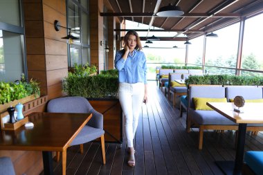 Fotoğraf modeli ayakta Café ve smartphone, kot gömlek ve beyaz pantolon giyen tutarak.