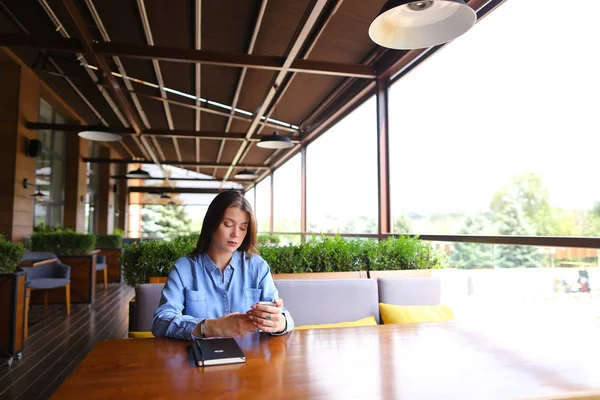 Estudiante sentada en la cafetería con portátil en la mesa y usando smartphone . — Foto de Stock