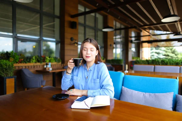 Caucásico persona femenina sentada en la cafetería con teléfono inteligente y portátil y beber café . — Foto de Stock