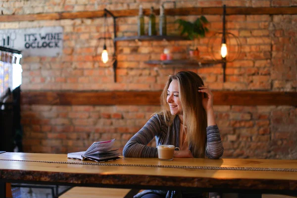 Hübsche Dame am Tisch mit Tasse Cappuccino und Notizbuch im gemütlichen Kaffeehaus. — Stockfoto