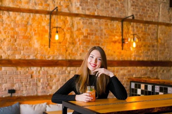 Chica satisfecha sentada cerca de la mesa de madera con taza de limonada en la cafetería y relajante . — Foto de Stock