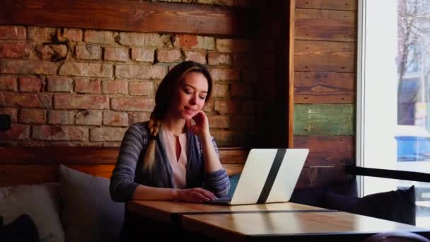 Söt flicka sitter på café och chatta med pojkvän av laptop. — Stockvideo