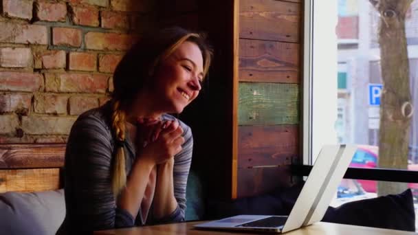 Mooie vrouw video bellen door laptop bij café, duimen opdagen en blazen kus. — Stockvideo