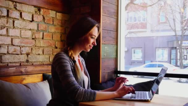 Mujer bonita escribiendo resumen por ordenador portátil en la cafetería . — Vídeo de stock