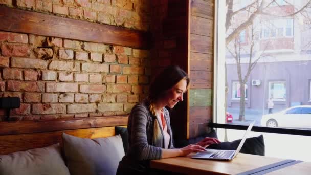 Ragazza Jocund chatta con ragazzo dal computer portatile al caffè vicino a una grande finestra . — Video Stock