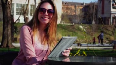 Çekici kız parkta tablet ve güneş gözlüğü dinlenme ile çalışma.