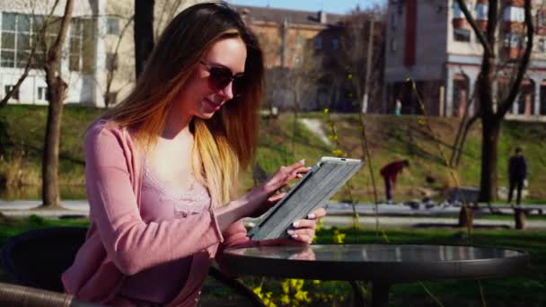 Young female person enjoying social networks in park and chatting by tablet. — Stock Video