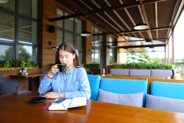 Nette Frau sitzt mit Smartphone und Notebook im Café und trinkt Kaffee. — Stockfoto