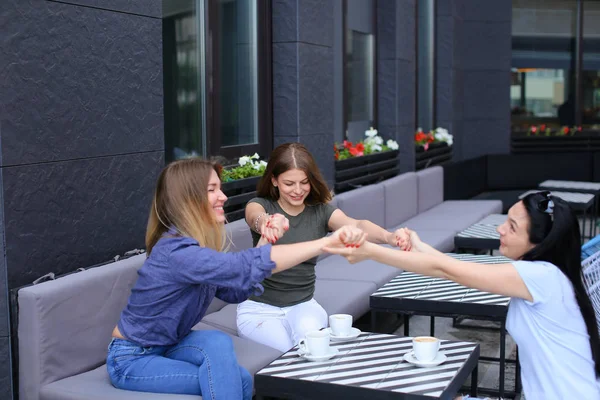 Sonrientes amigas sentadas en la cafetería y cogidas de la mano . — Foto de Stock