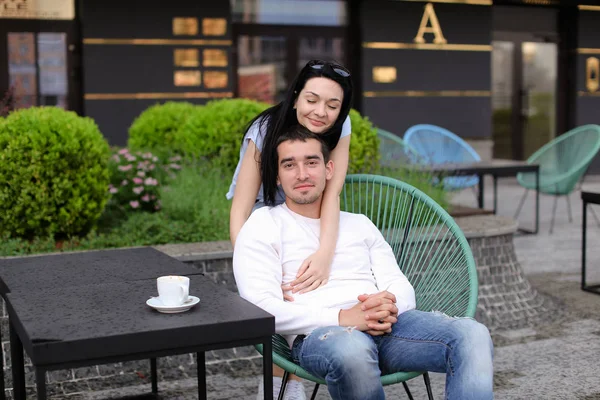 Glückliche Frau umarmt Ehemann sitzt im Stuhl im Straßencafé draußen. — Stockfoto