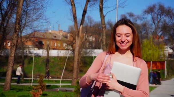 Ganska leende flicka promenera i parken med smartphone och laptop. — Stockvideo