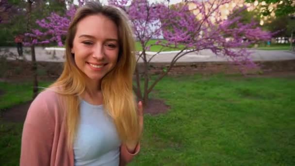 Close up smile of pretty woman walking with blooming tree background in slow motion. — Stock Video