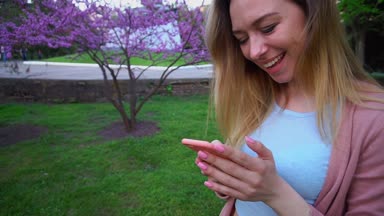 Smartphone tarafından sohbet ve çiçek açan park, yavaş yürüyen genç bir kadın.