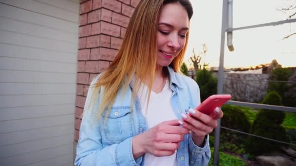 Jong meisje met close-up typen handen door smartphone staande in de buurt van garage. — Stockvideo