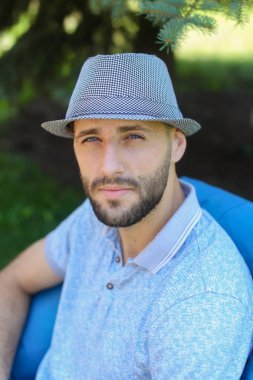 Çanta sandalyede oturan ve mavi şapka giyen genç adam.